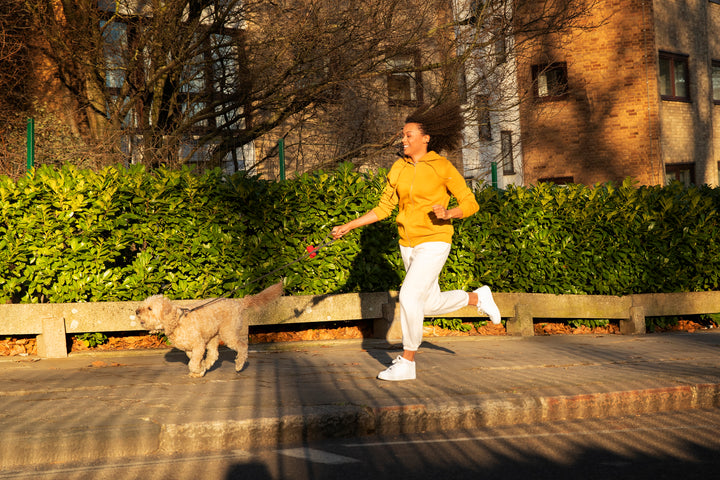 A woman in a morning walk outfit running with her dog on a sunny day